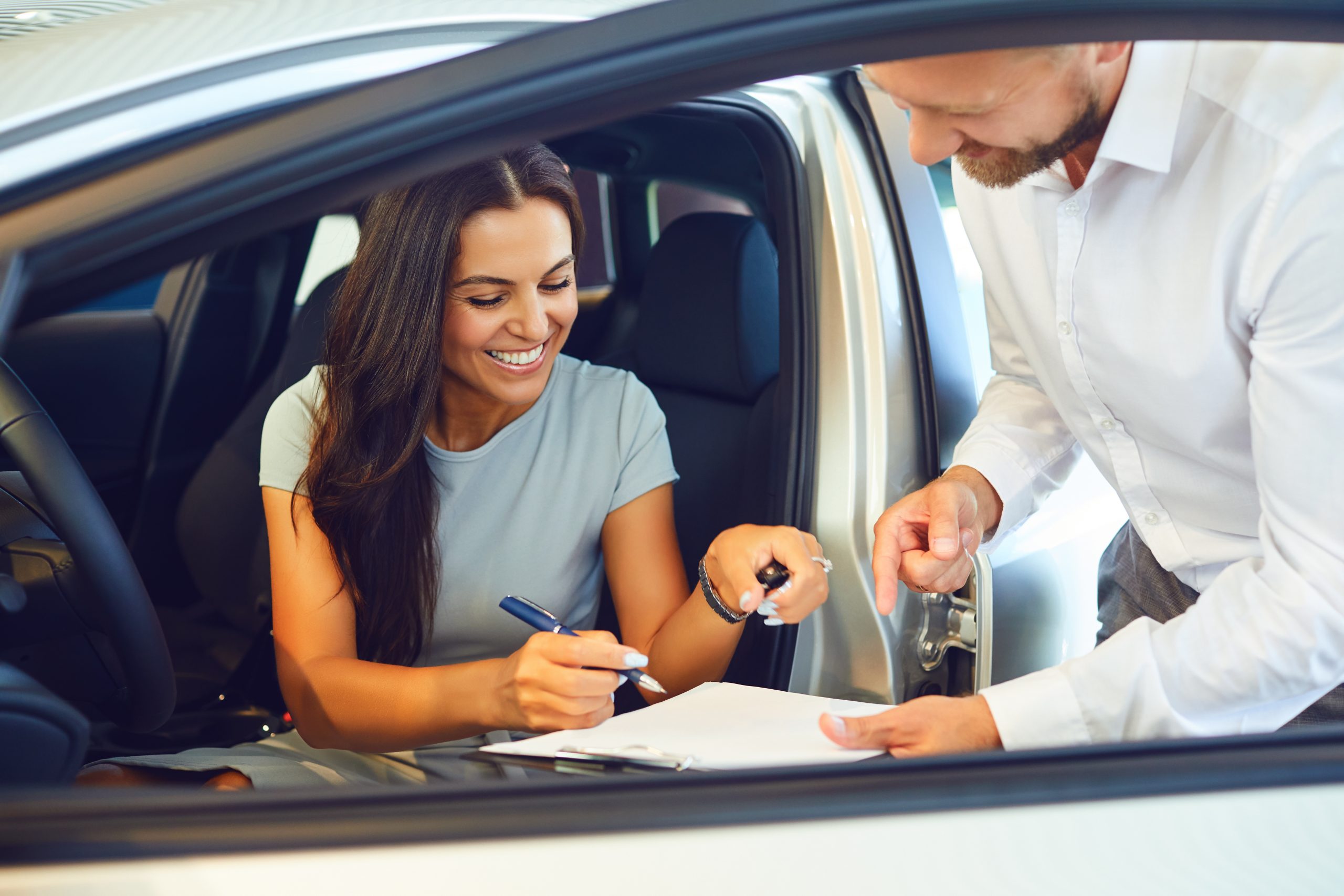 A young woman buys a car in a car showroom. A man signs a car agreement.