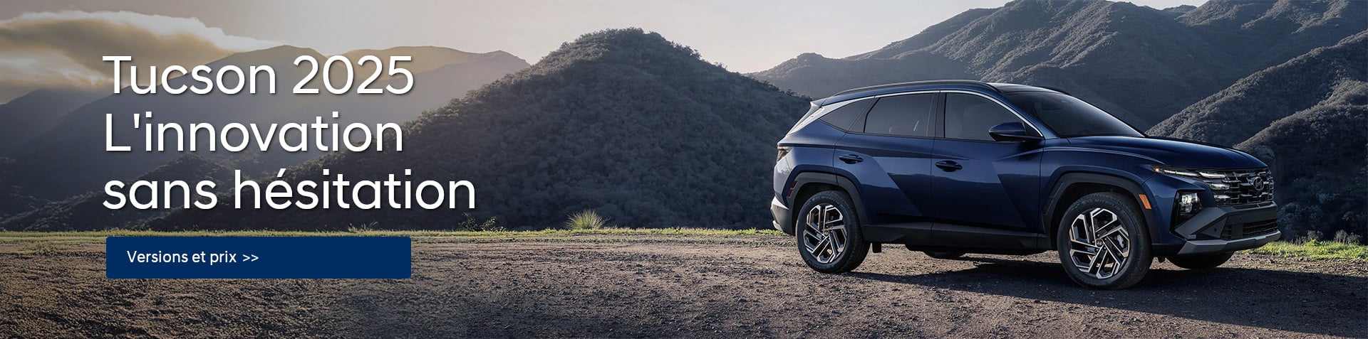 Un Tucson 2025 bleu foncé est stationné sur une route de terre avec des montagnes en arrière plan