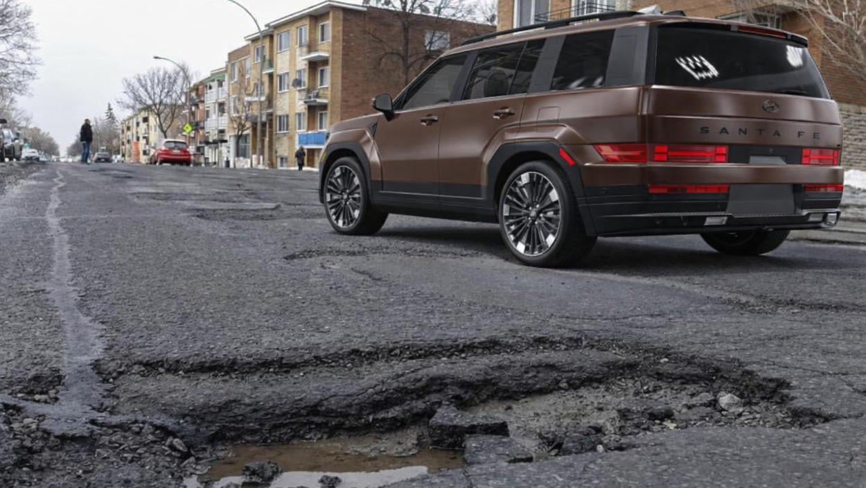 Brown 2026 Hyundai Santa Fe driving over a pothole-damaged city street, illustrating the SUV’s capability in harsh Quebec road conditions.
