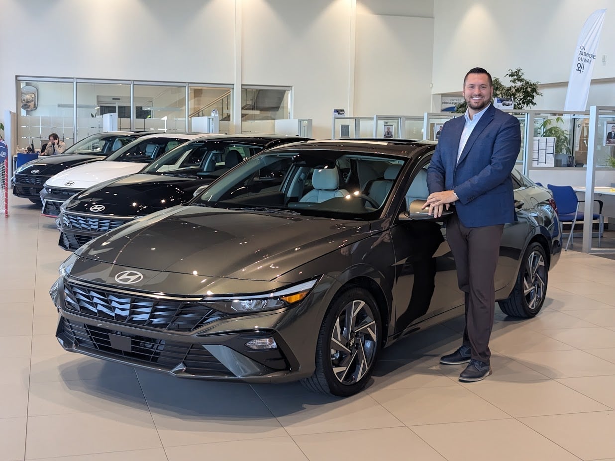Daniel-Alexandre Goupil Grisé, spécialiste des véhicules électriques et hybrides, avec le Hyundai ELANTRA hybride 2026 Gris Amazone devant Brossard Hyundai.