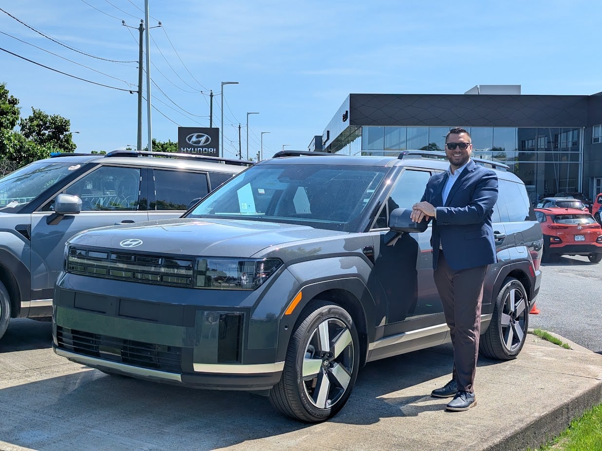 Daniel-Alexandre Goupil Grisé, spécialiste des véhicules électriques et hybrides, avec le Hyundai SANTA FE hybride 2026 Gris Écotronique devant Brossard Hyundai.