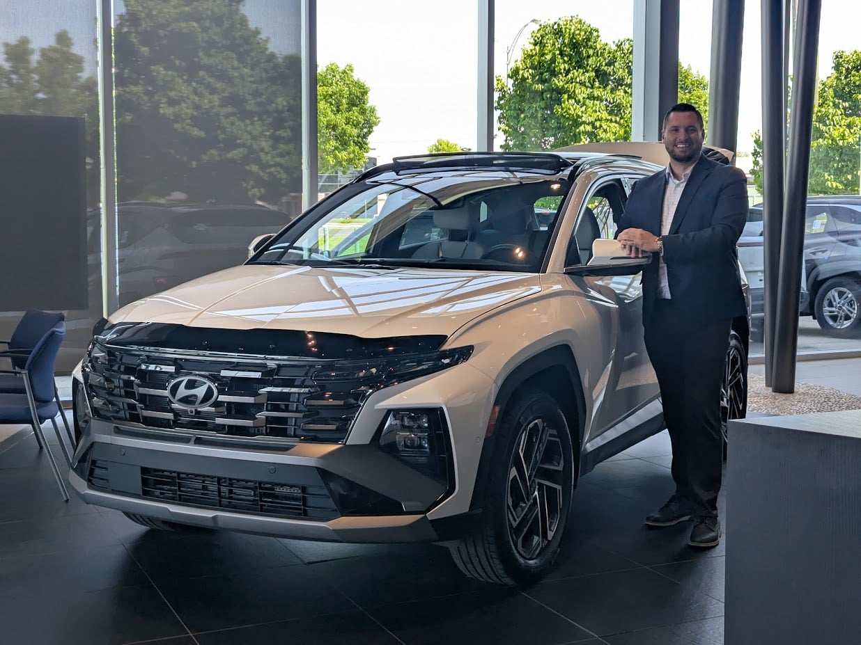 Daniel-Alexandre Goupil Grisé, spécialiste des véhicules électriques et hybrides, avec le Hyundai TUCSON hybride 2026 Blanc Cristal devant Brossard Hyundai.