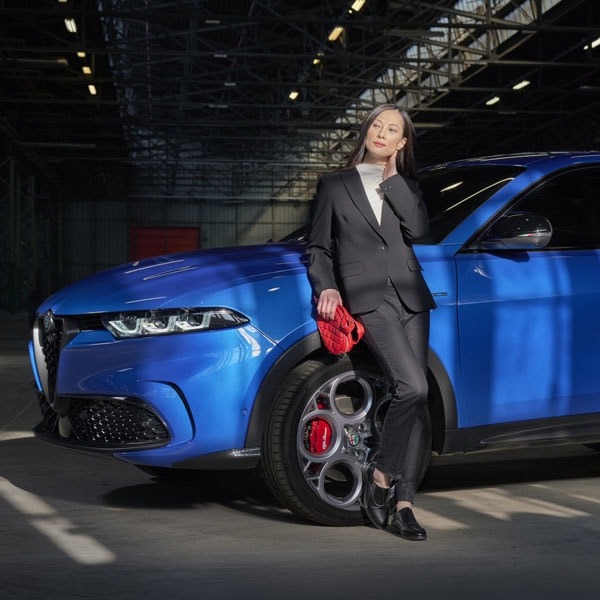 Lady leaning against Alfa Romeo Tonale with red purse in hand.